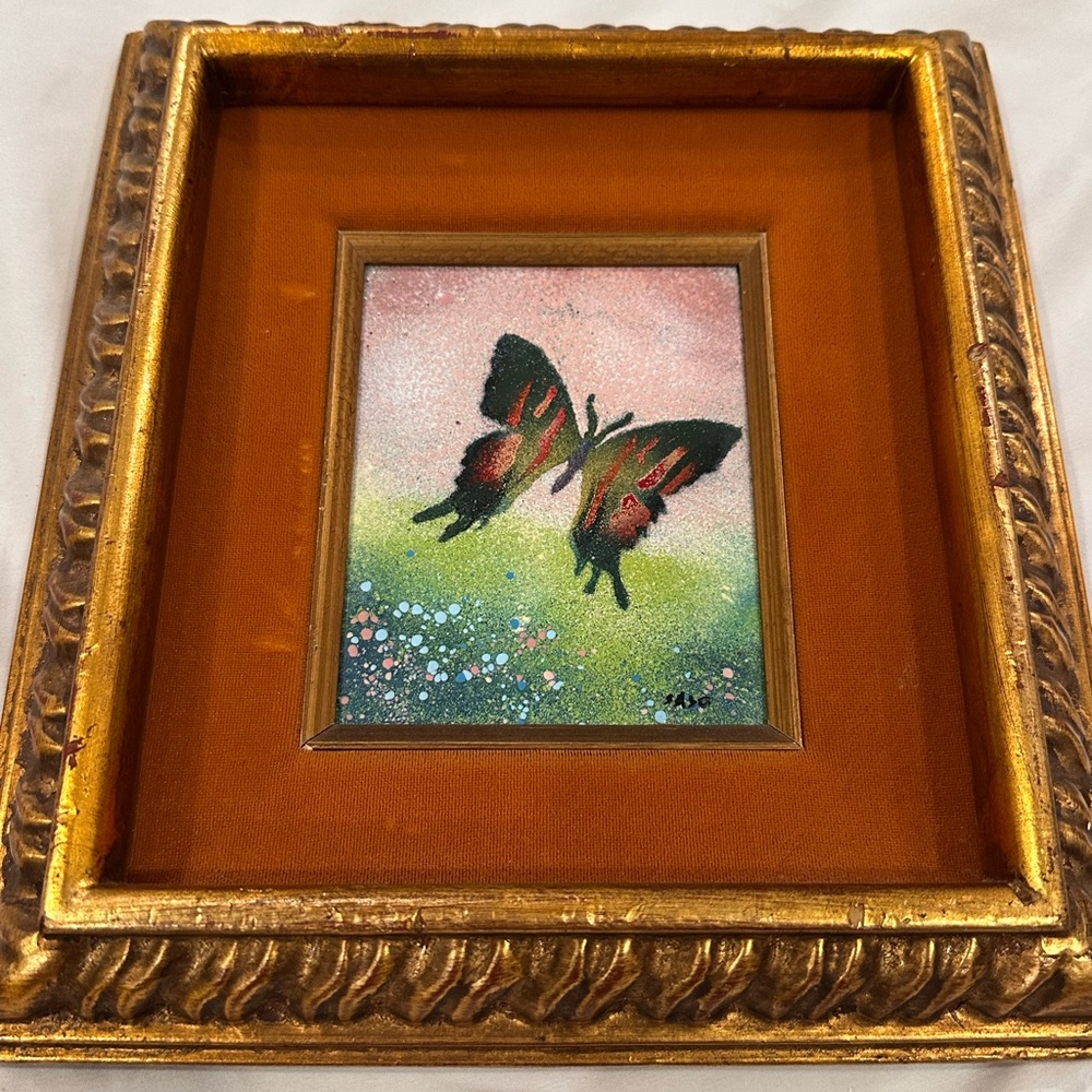 Hand-painted enamel depicting a butterfly floating over a field of flowers.